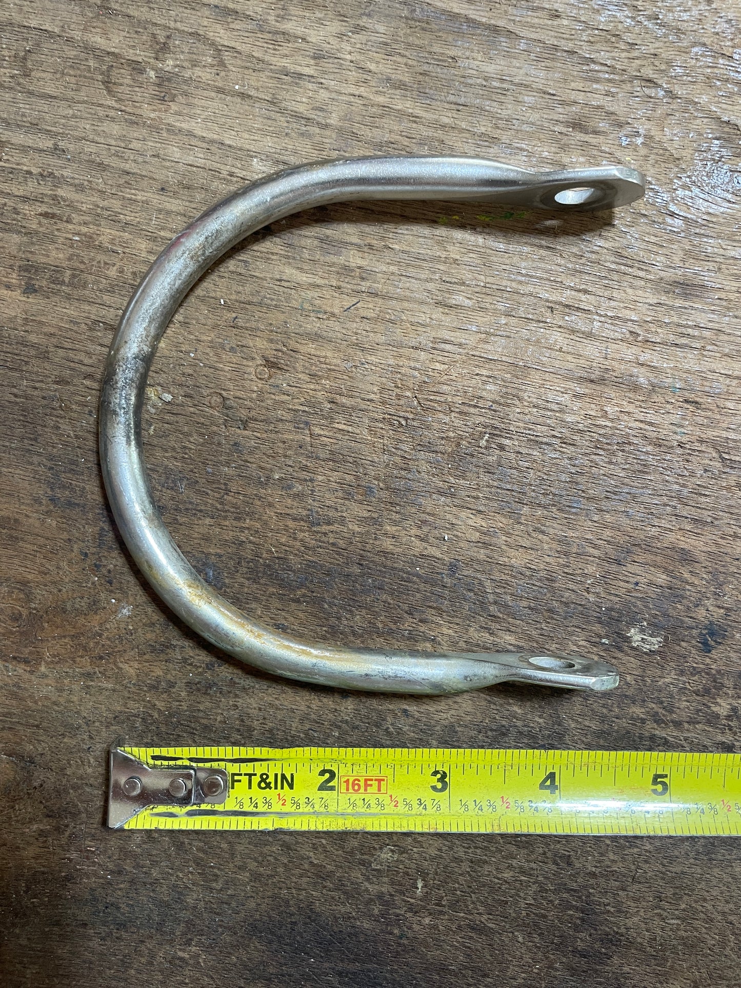 Metal fish hook on a wooden surface with a tape measure for scale.