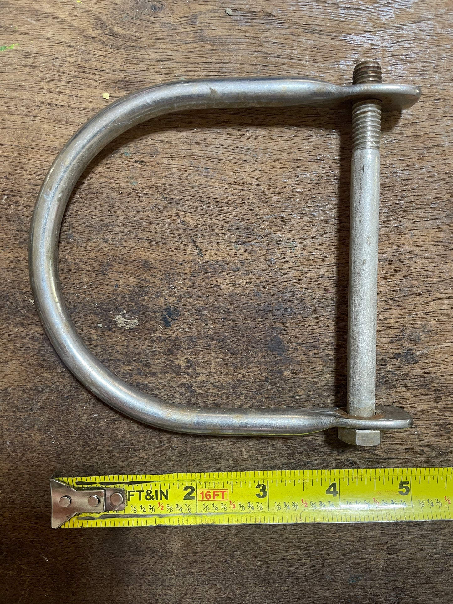 Metal U-bolt on a wooden surface with a tape measure for scale.