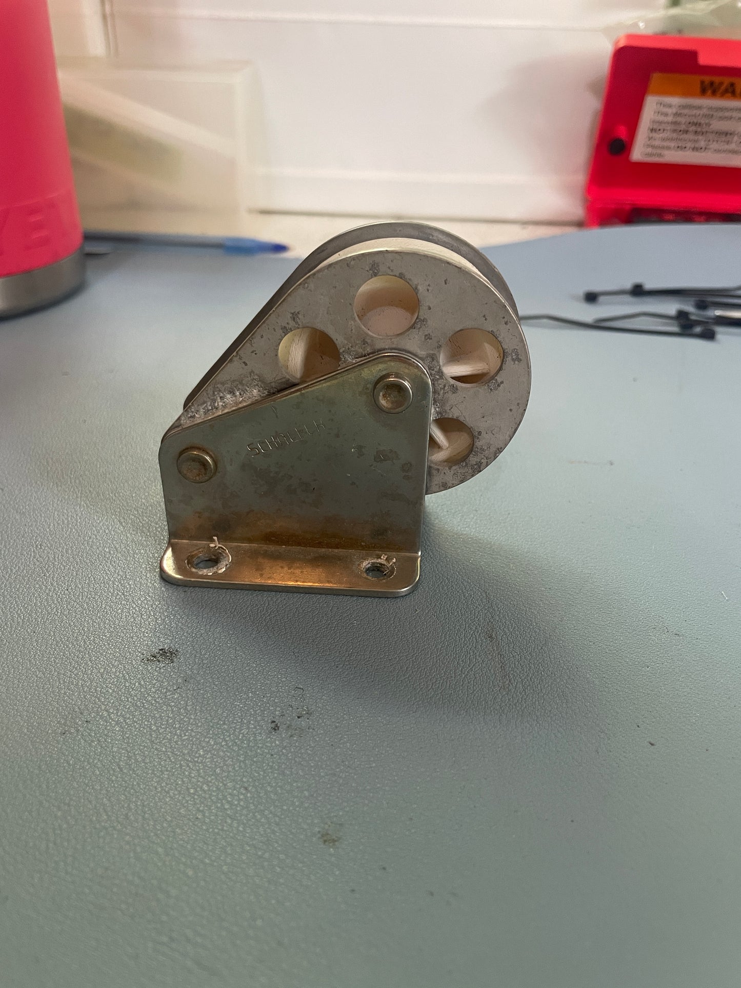 Metal pulley system attached to a wall with a red tool in the foreground.
