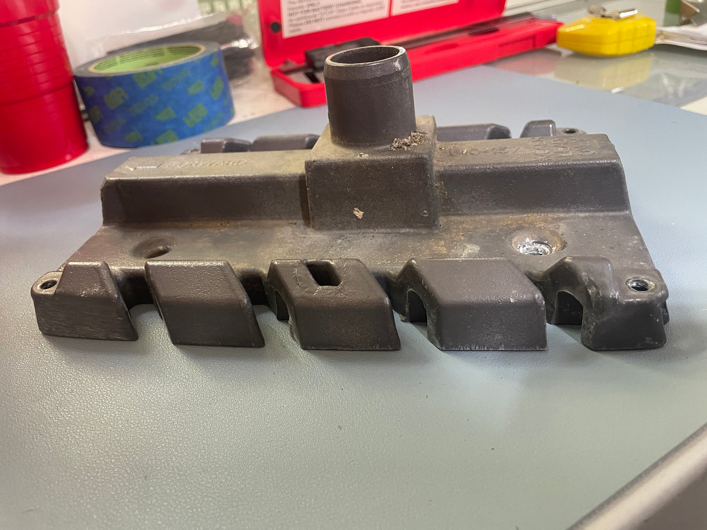 Metal component on a gray surface with tools in the background