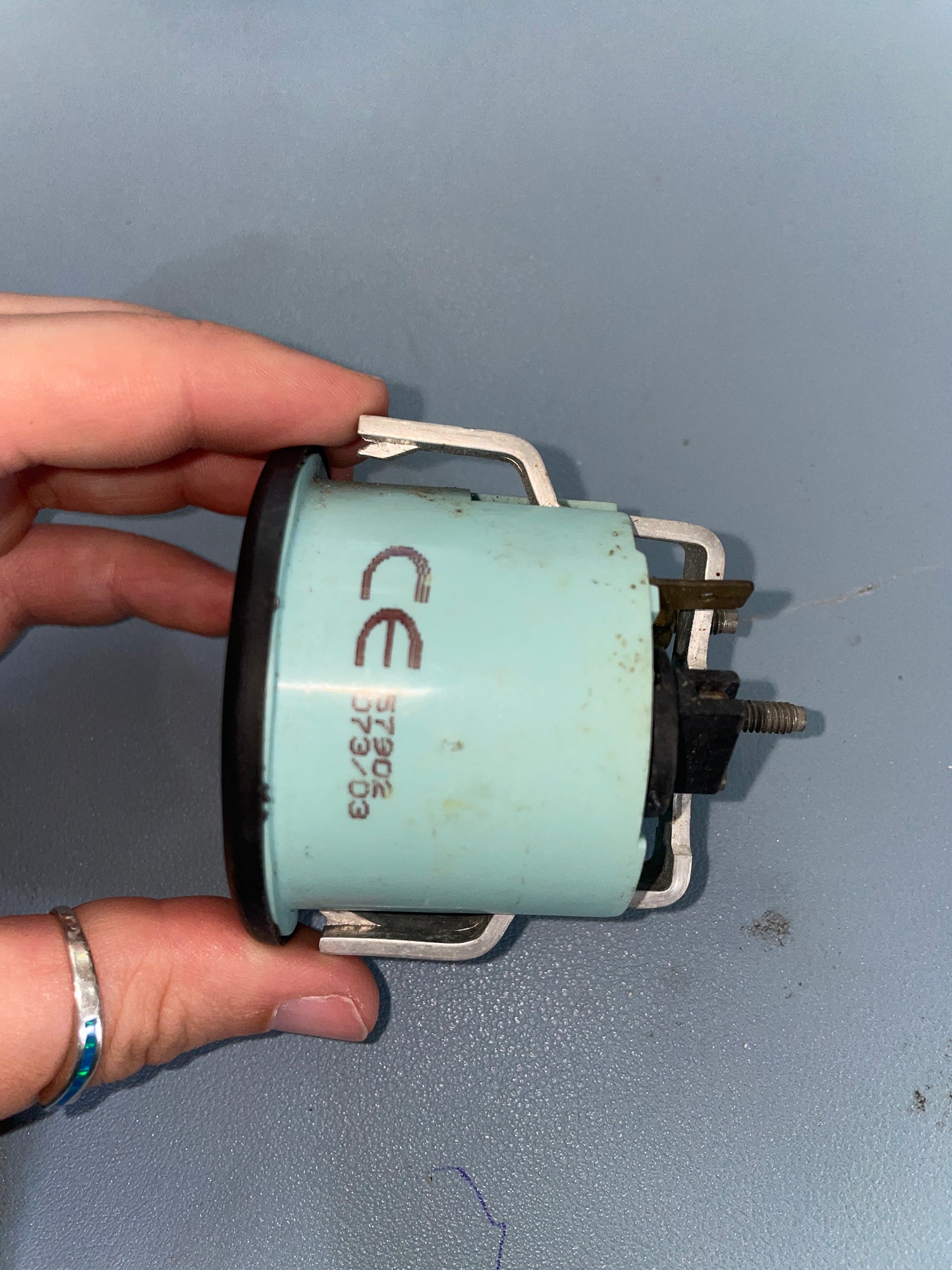 Hand holding a cylindrical mechanical component with 'CE' marking against a gray background