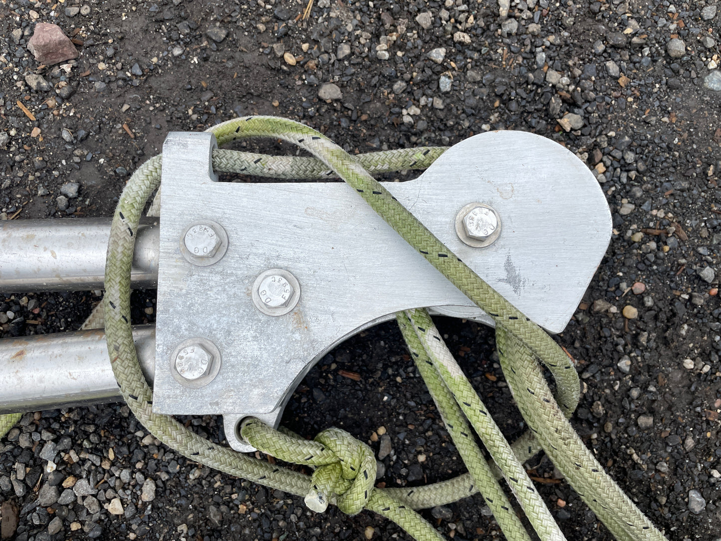 Metal knotting tool with green rope on a gravel surface