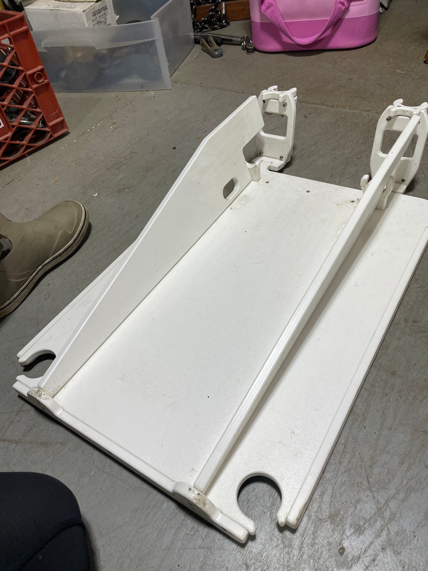 White metal bracket on a concrete floor with a pink object and plastic container in the background.
