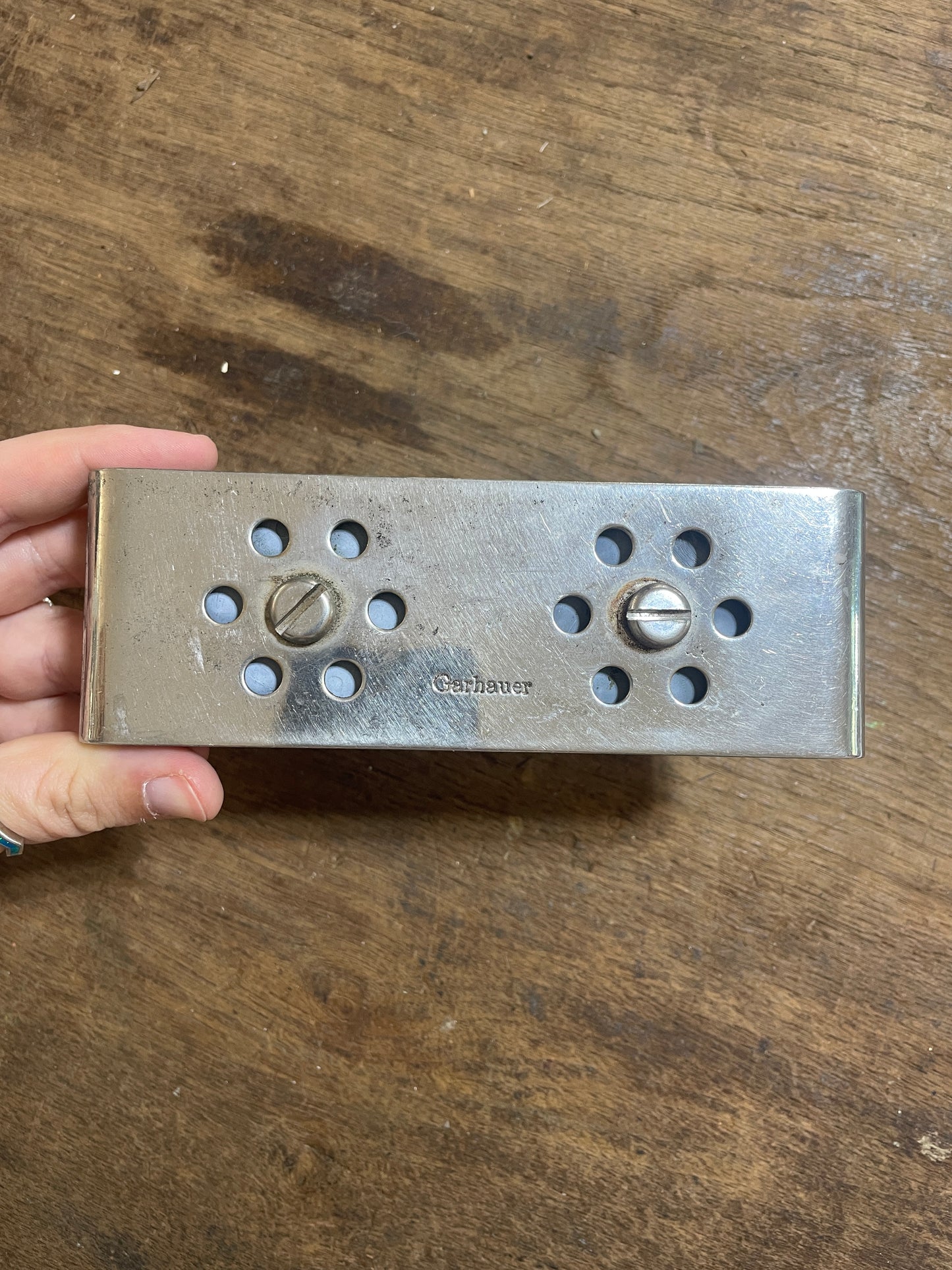 Metal door handle plate held by a hand on a wooden surface