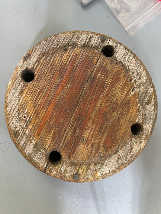 Round wooden object with four holes on a light gray background