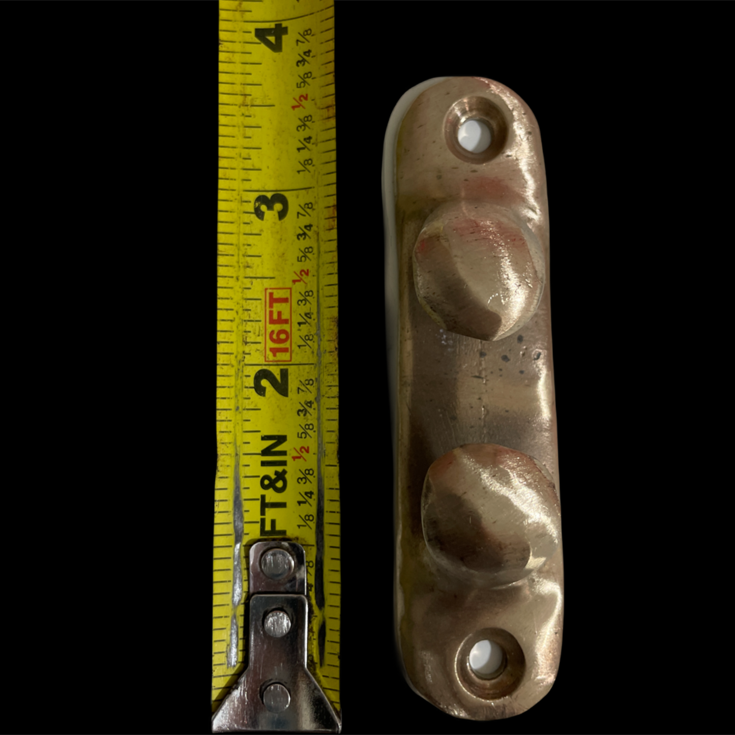 Metallic handle with three circular indentations next to a measuring tape on a black background