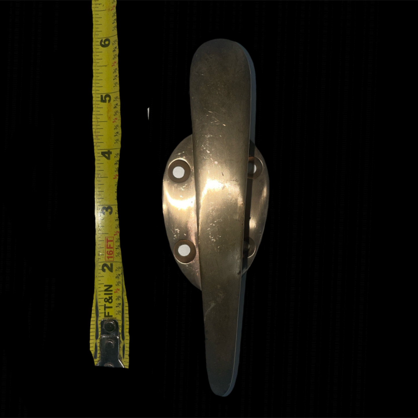 Metal window handle with a tape measure for scale on a black background