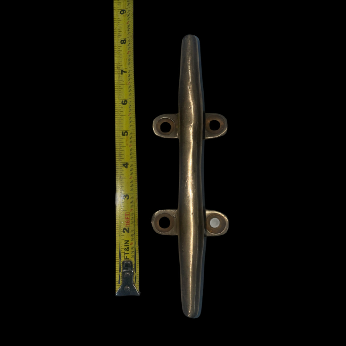 Metal cleat with a tape measure for scale on a black background
