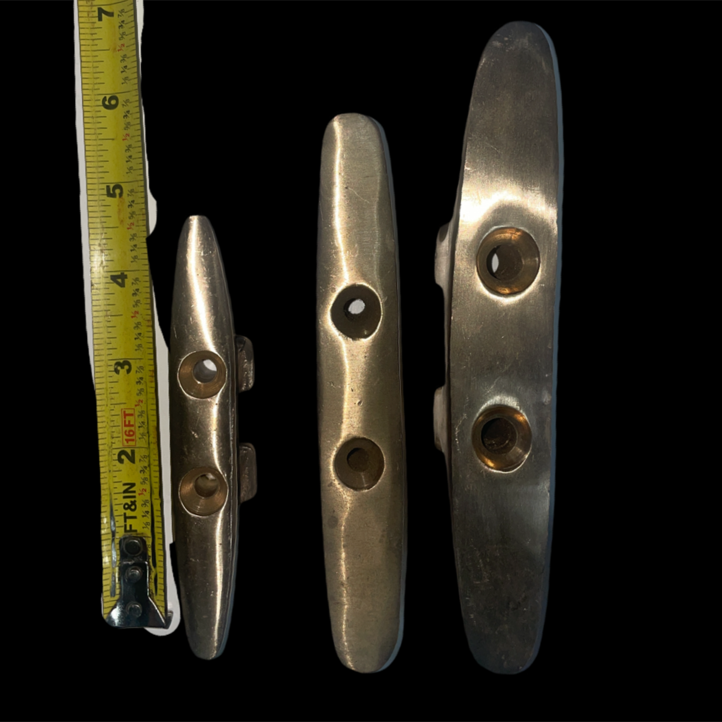 Three metal cleats with a tape measure for scale on a black background