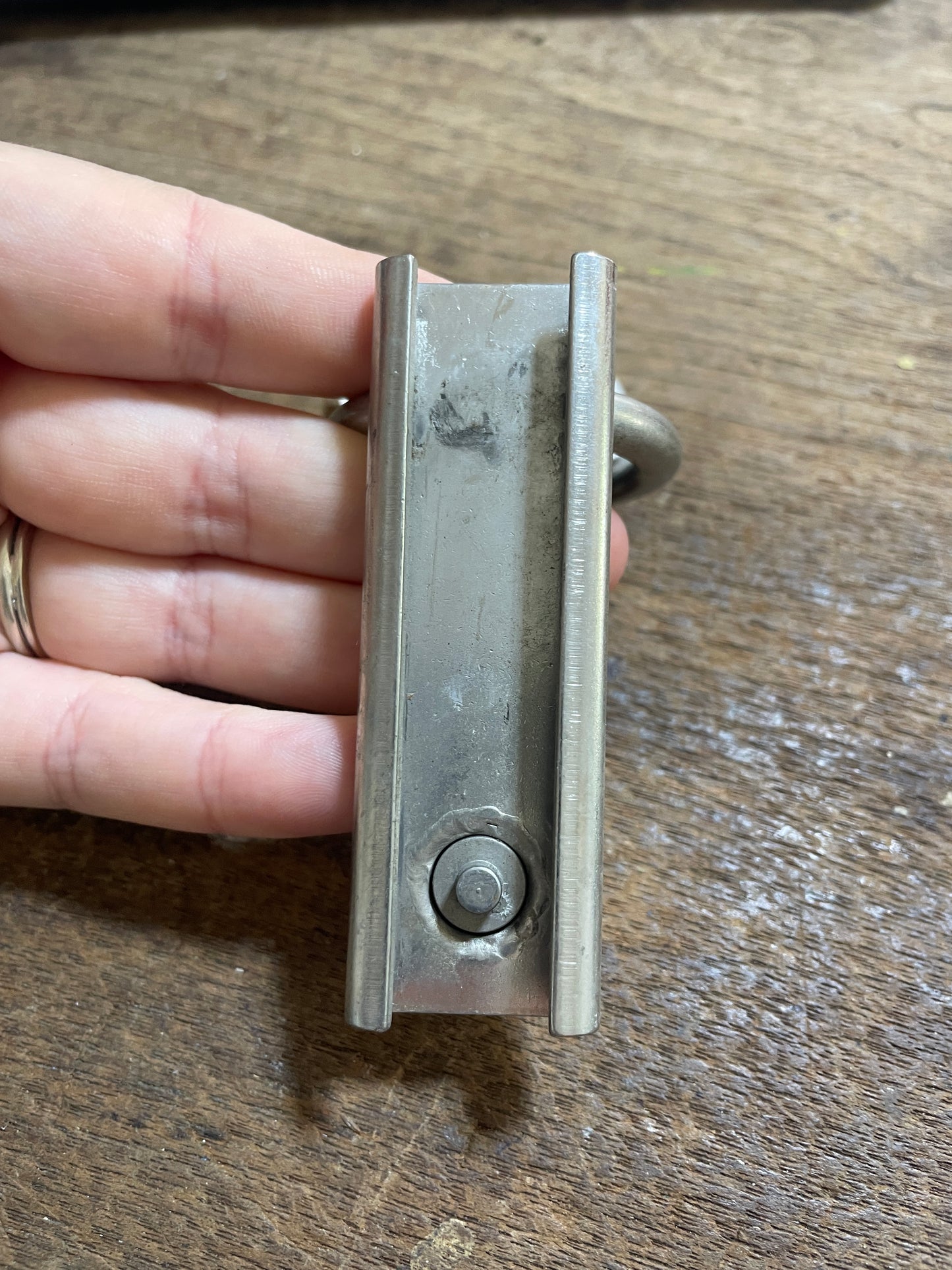 Metal bracket held by a hand against a wooden background