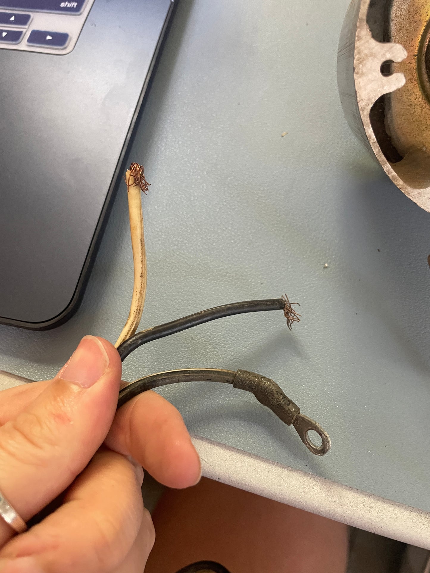 Hand holding a damaged electrical wire near a laptop on a gray surface
