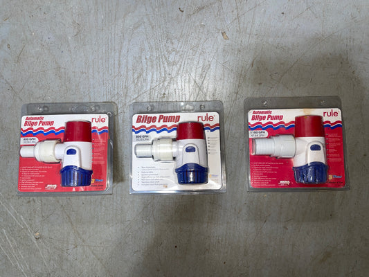 Three packages of Rule bilge pumps on a gray surface