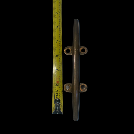 Metal cleat with a tape measure for scale on a black background