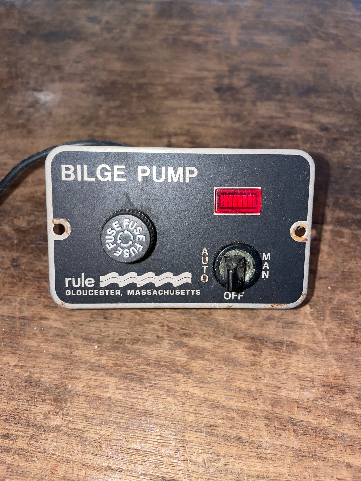 Bilge Pump Control Switch with a black casing, white labels, red on/off switch, and connected by a black wire.