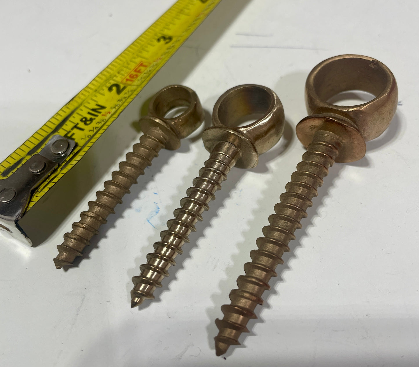 Three brass screws on a white surface with a tape measure for scale.