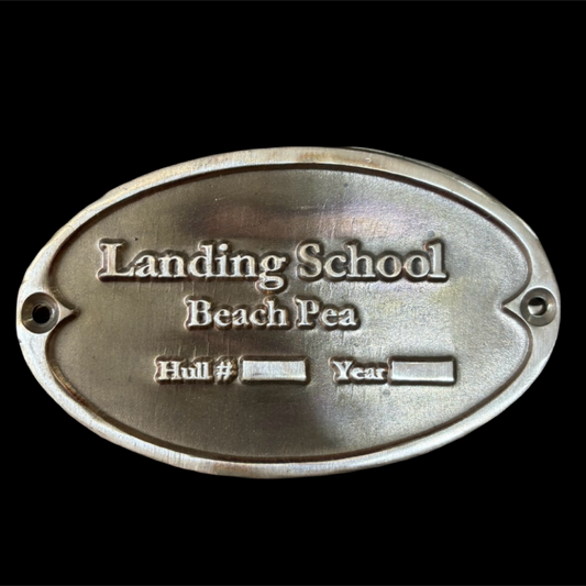 Metal plaque with 'Landing School Beach Pea' text on a black background