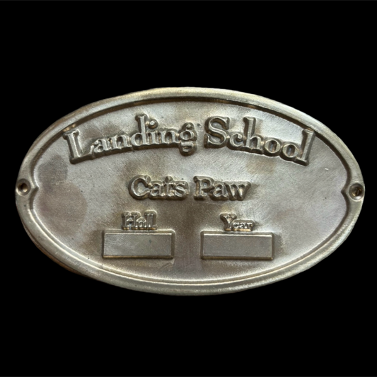 Metal plaque with 'Landing School Cats Paw' text on a black background