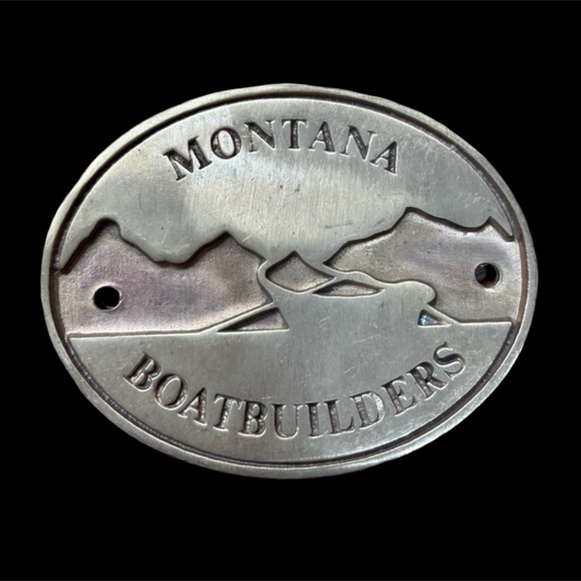Metal badge with 'Montana Boatbuilders' text and logo on a black background