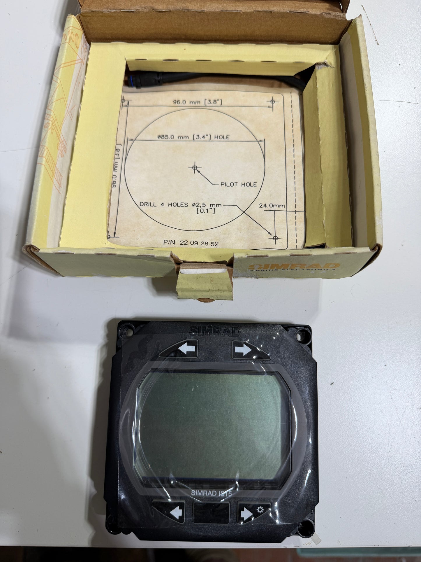 Electronic component on a white surface next to an open cardboard box with technical drawings.