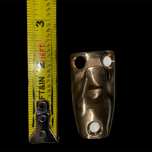 Brass bracket with two holes next to a yellow measuring tape on a black background