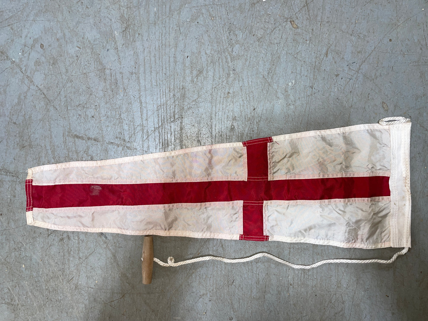 Small flag with a red cross on a white background, attached to a wooden stick on a gray surface.