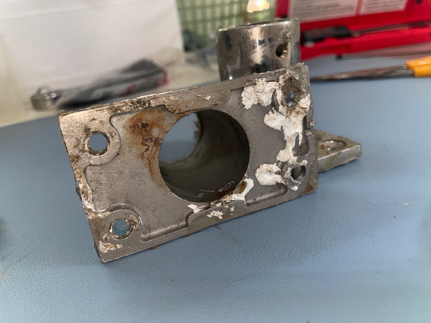 Worn metal bracket on a blue surface with tools in the background