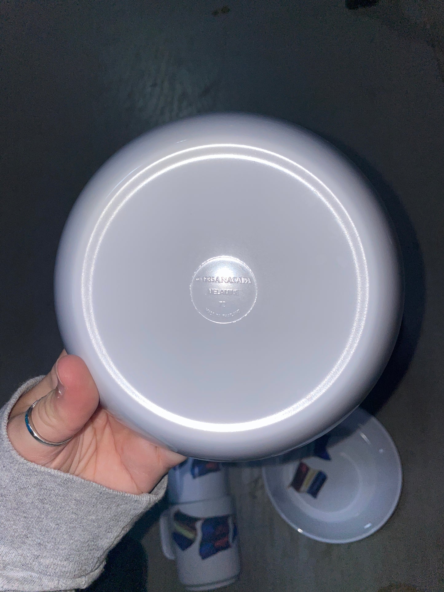 Hand holding a white lid with a brand logo on a dark surface