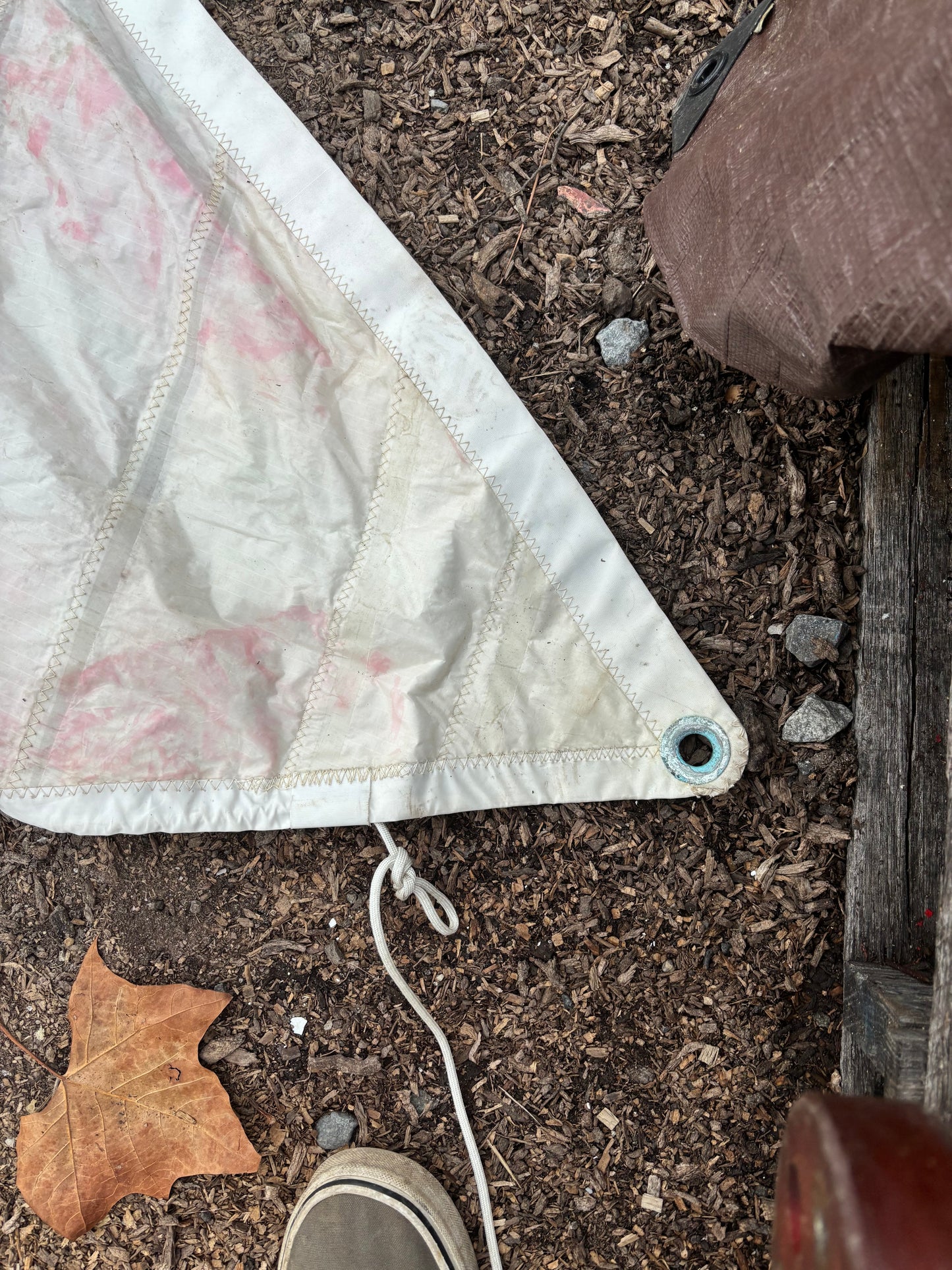 White tarp on the ground with a small eyelet, surrounded by dirt and leaves.