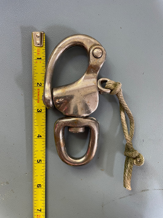 Metal shackle with a rope on a gray surface, measured by a yellow tape measure.