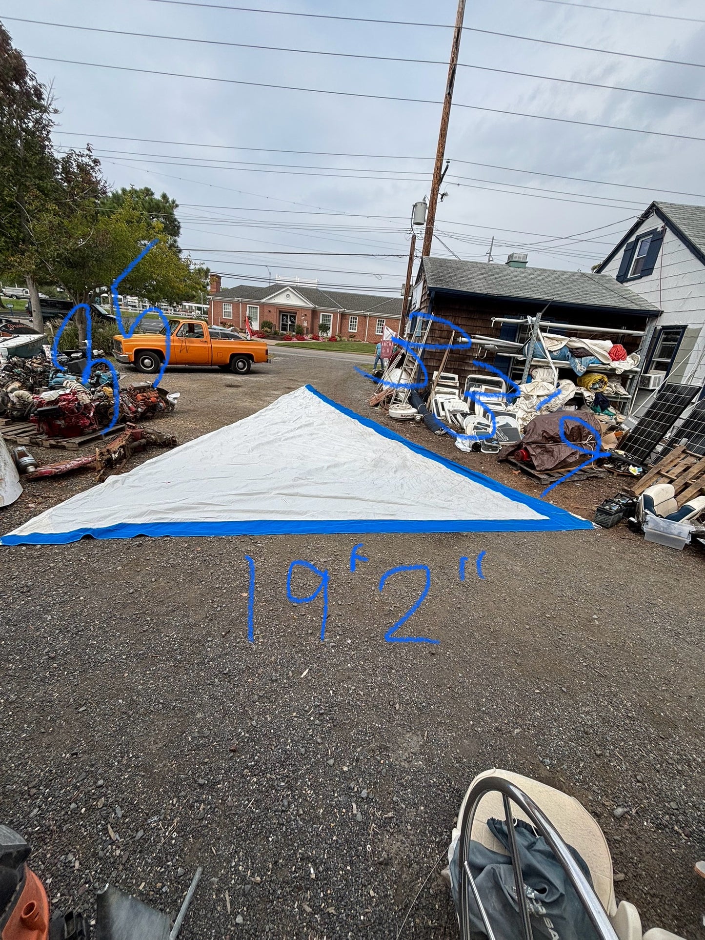 Large white and blue tarp on the ground with measurements, set against a backdrop of a residential area with houses and cars.