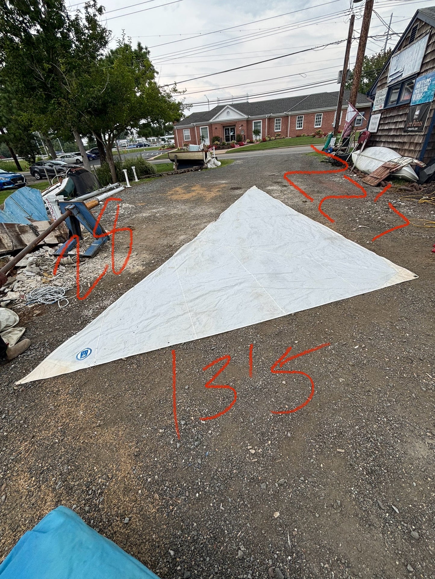 Large white triangle-shaped mat on a street with measurements written on it, surrounded by trees and buildings.