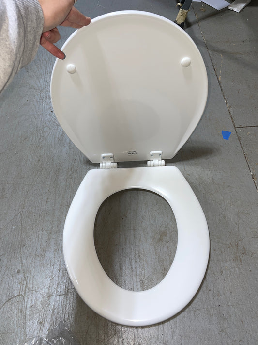 White toilet seat on a gray floor with a hand holding it open.