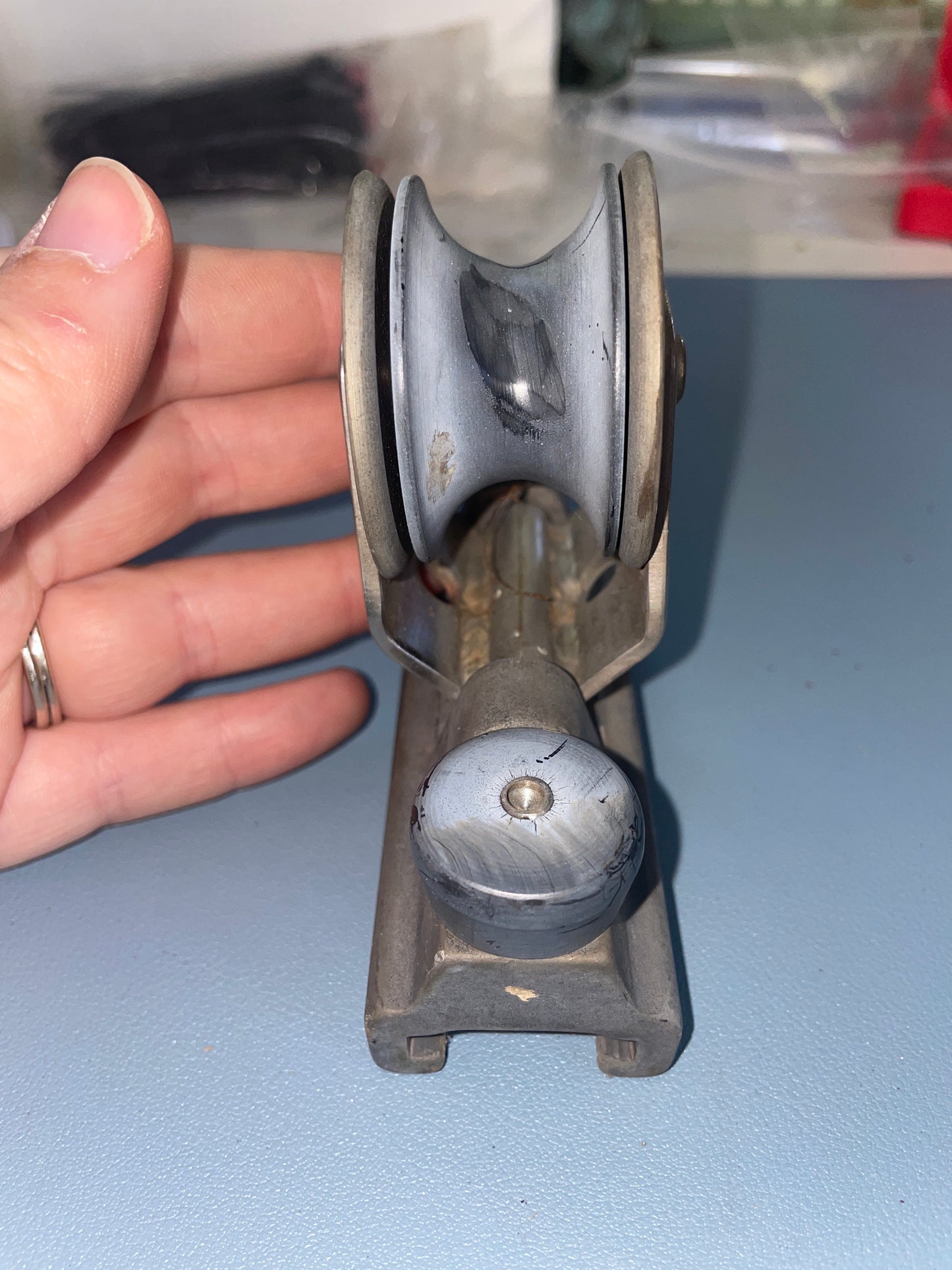 Metal pulley system held by a hand against a light blue wall.