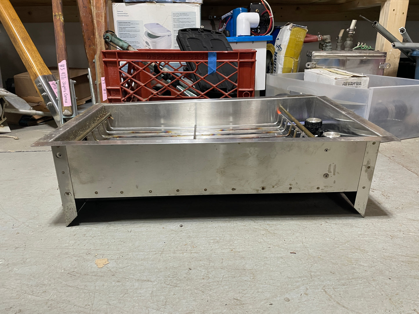 Stainless steel sink in a workshop setting with tools and equipment in the background.