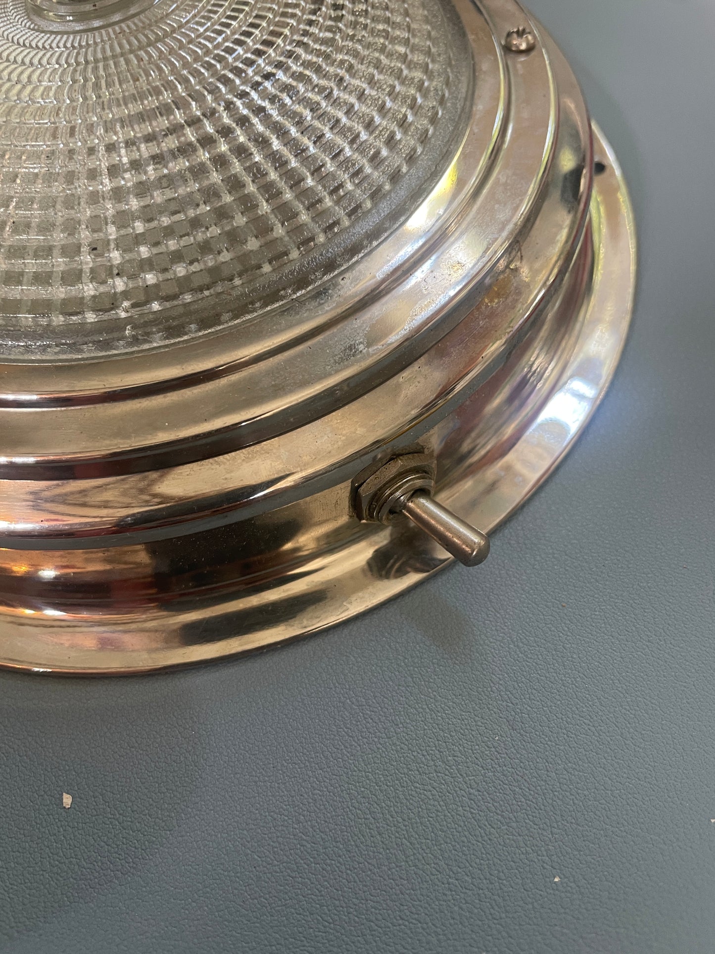 Round metallic light fixture with glass cover on a gray wall