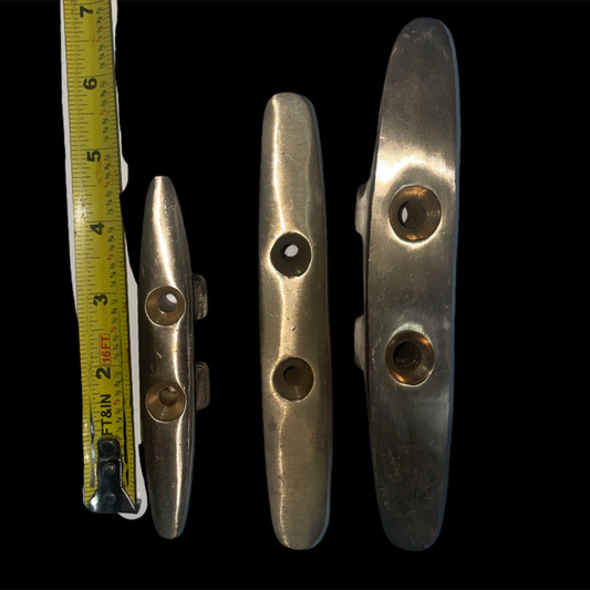 Three metal cleats with a tape measure for scale on a black background