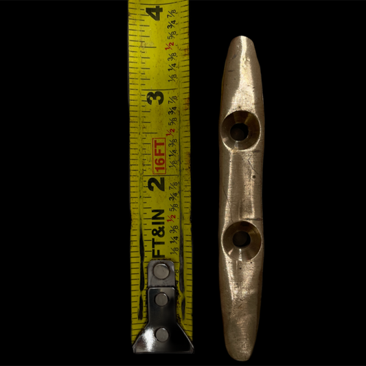 Metal cleat with two holes next to a tape measure on a black background
