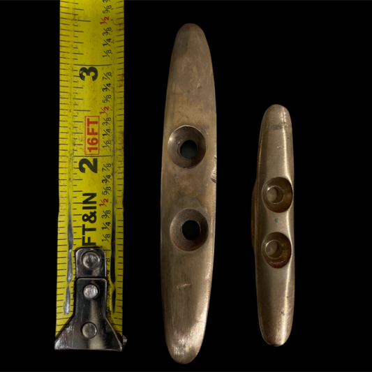 Two metal boat cleats with a measuring tape for scale on a black background
